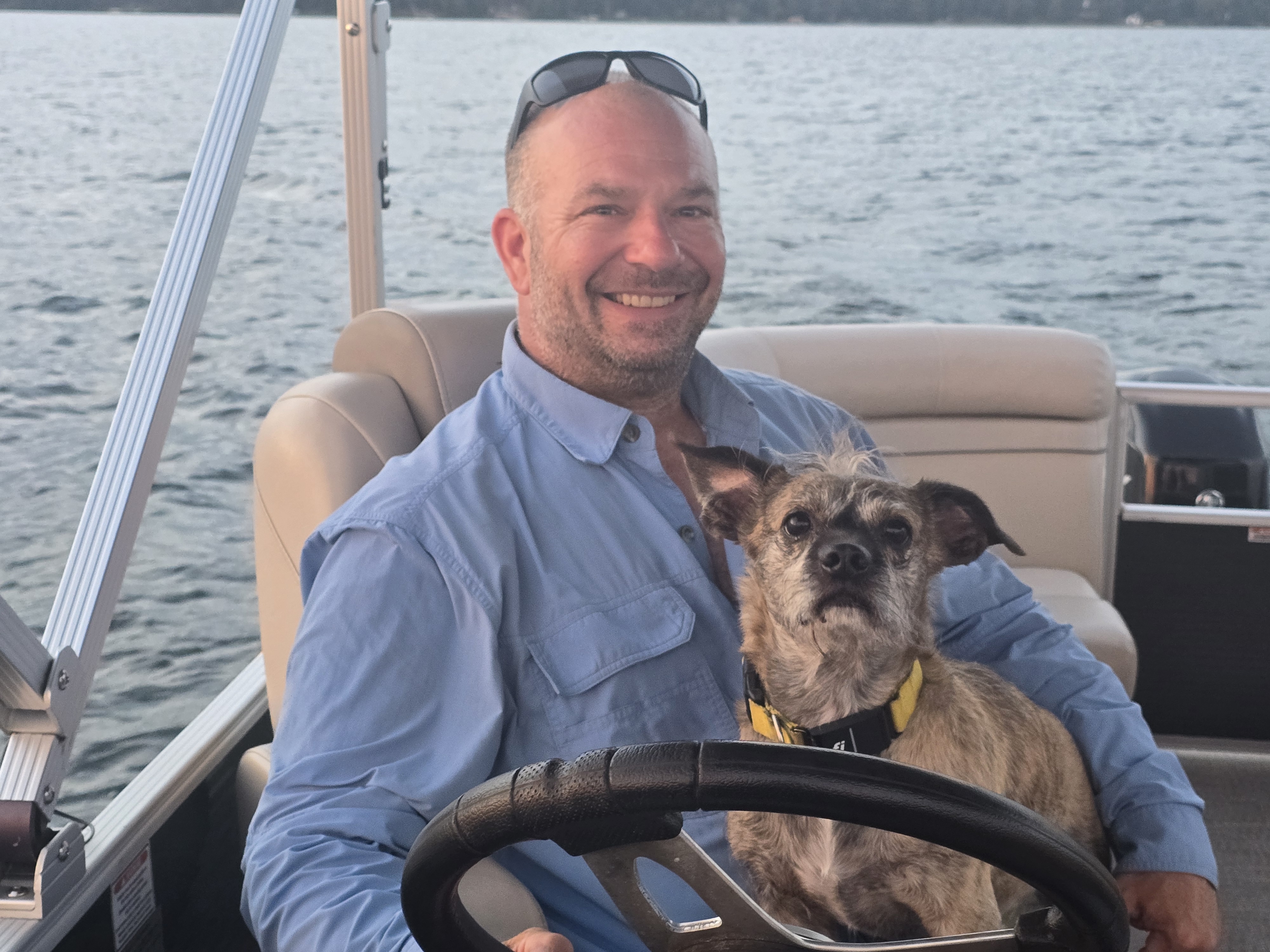 Matt smiling at the wheel of a boat with a dog on his lap.